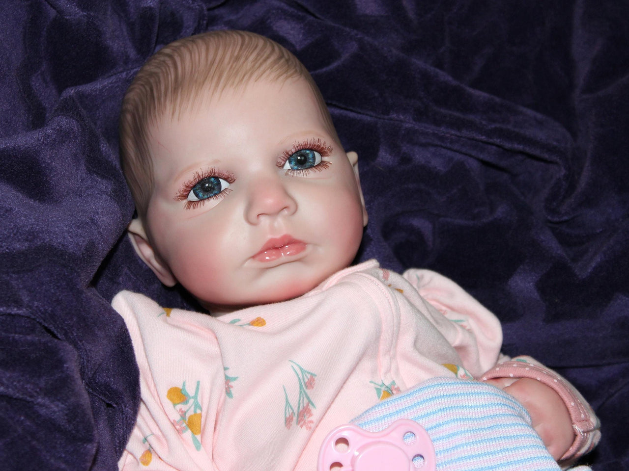 Realistic reborn baby doll dressed in pink floral pajamas with pacifier, cuddly lifelike doll for kids to play and nurture