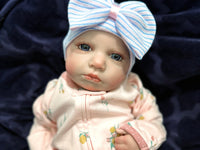 Thumbnail for Lifelike reborn baby doll with blue eyes wearing a pink floral outfit and striped bow hat, realistic weighted newborn therapy doll