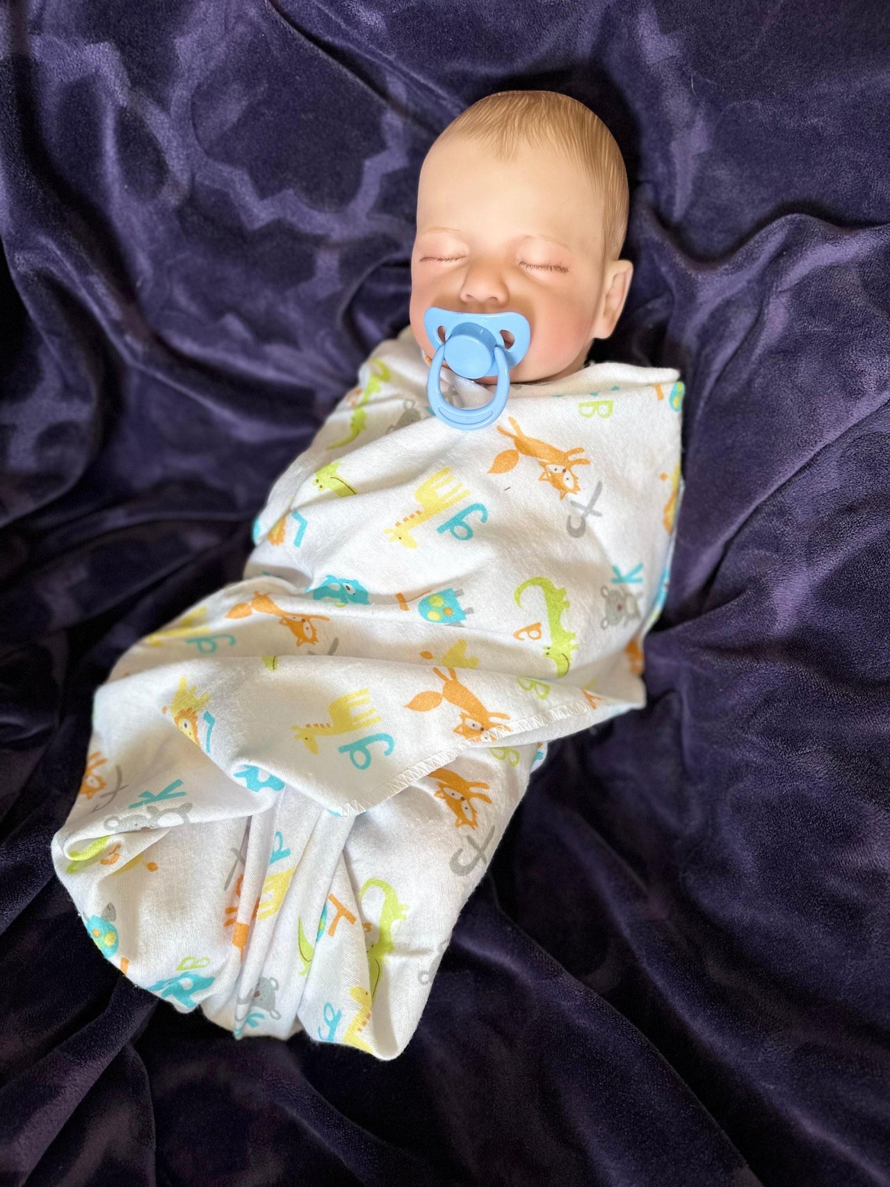 Sleeping reborn baby doll swaddled in animal print blanket with blue pacifier, lifelike handmade newborn doll for collectors or therapy