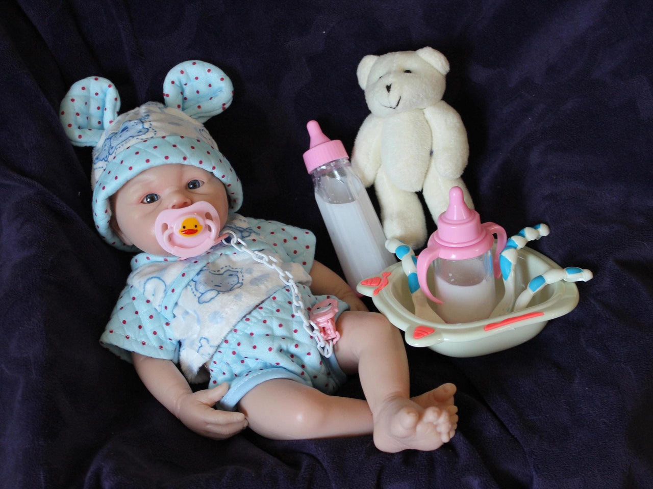 Lifelike reborn baby doll with blue eyes wearing blue bear-print outfit and matching bunny ear hat, realistic handmade newborn doll