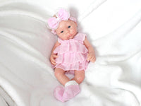 Thumbnail for A baby doll in a pink dress and headband, showcasing a cheerful expression and delicate features.
