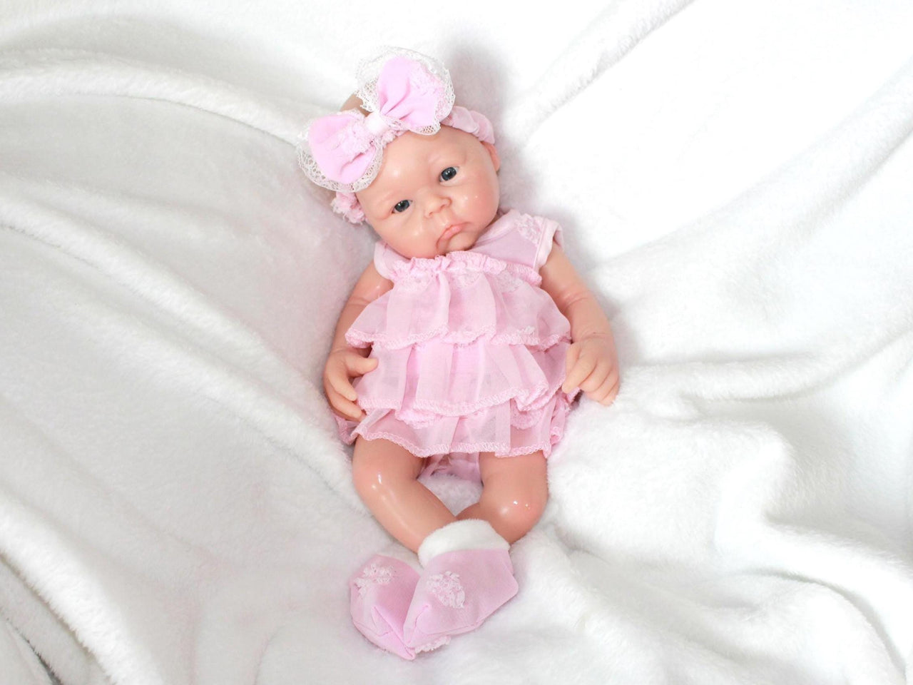 A baby doll in a pink dress and headband, showcasing a cheerful expression and delicate features.