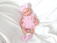 Thumbnail for A baby doll in a pink dress and headband, showcasing a cheerful expression and delicate features.