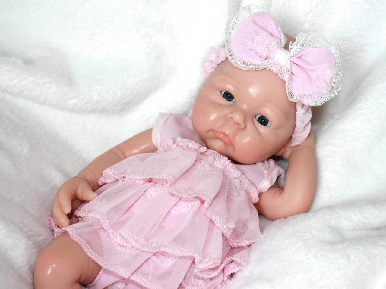 A baby doll in a pink dress and headband, showcasing a cheerful expression and delicate features.