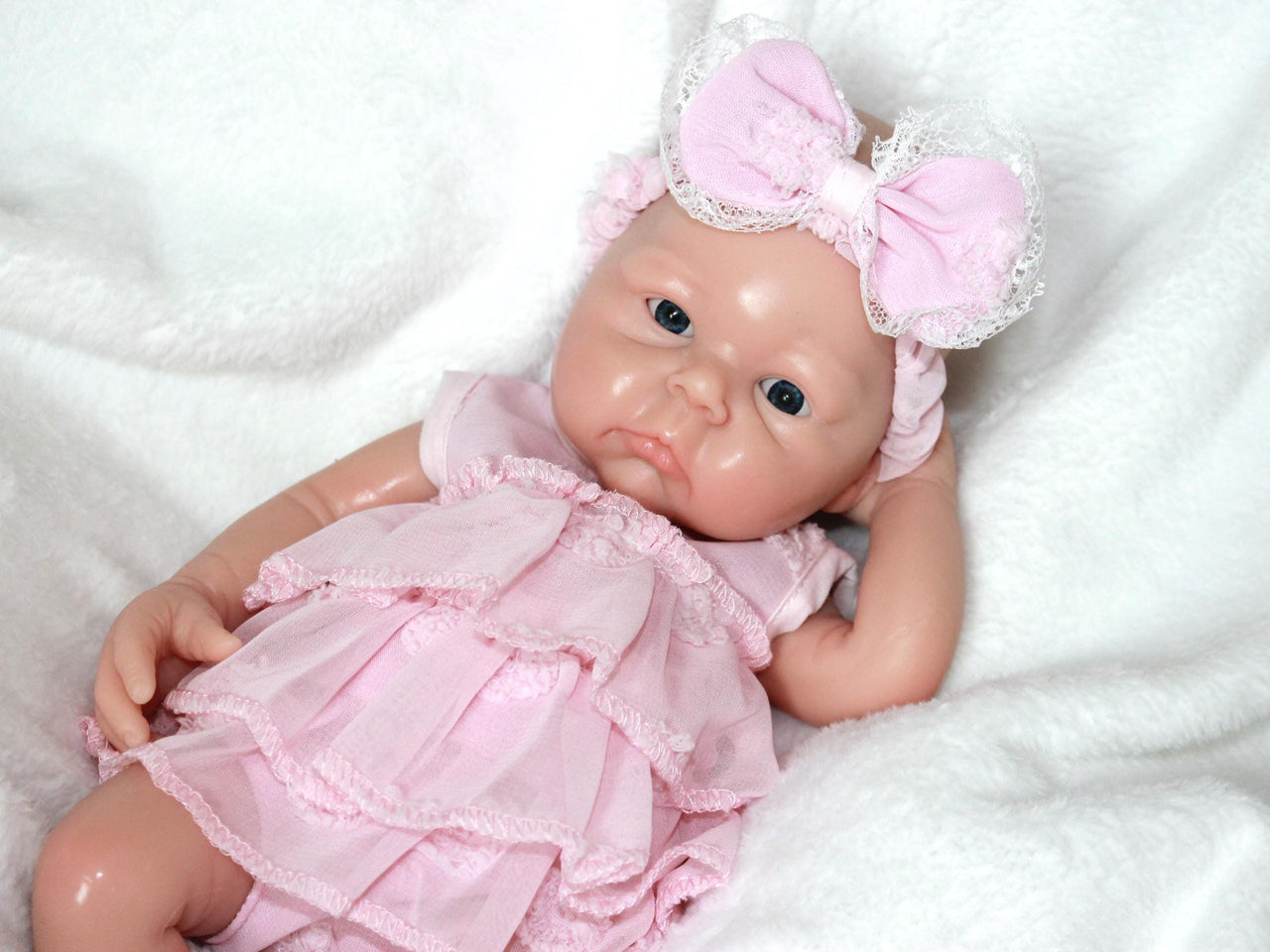 A baby doll dressed in a pink dress and matching headband, sitting against a soft background.
