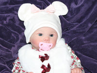 Thumbnail for A baby doll resting on a purple sheet, showcasing its soft features and delicate clothing.