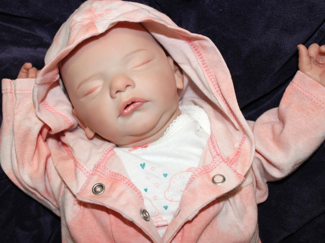 A baby doll peacefully sleeps on a soft white blanket, creating a serene and cozy scene.