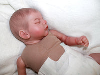 Thumbnail for A baby doll peacefully sleeps on a soft white blanket, creating a serene and cozy scene.