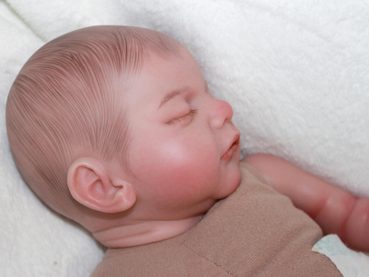 A baby doll lies asleep on a pristine white blanket, embodying tranquility and comfort.