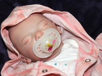 Thumbnail for A baby doll lies asleep on a pristine white blanket, embodying tranquility and comfort.