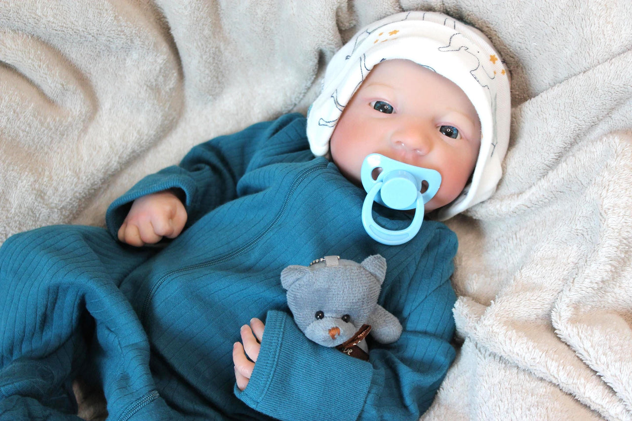 A baby doll with a pacifier in its mouth, featuring soft facial features and a teal outfit.