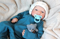 Thumbnail for A baby doll with a pacifier in its mouth, featuring soft facial features and a teal outfit.