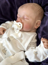 Thumbnail for A baby doll lying on a cozy blanket, with a pacifier placed nearby.