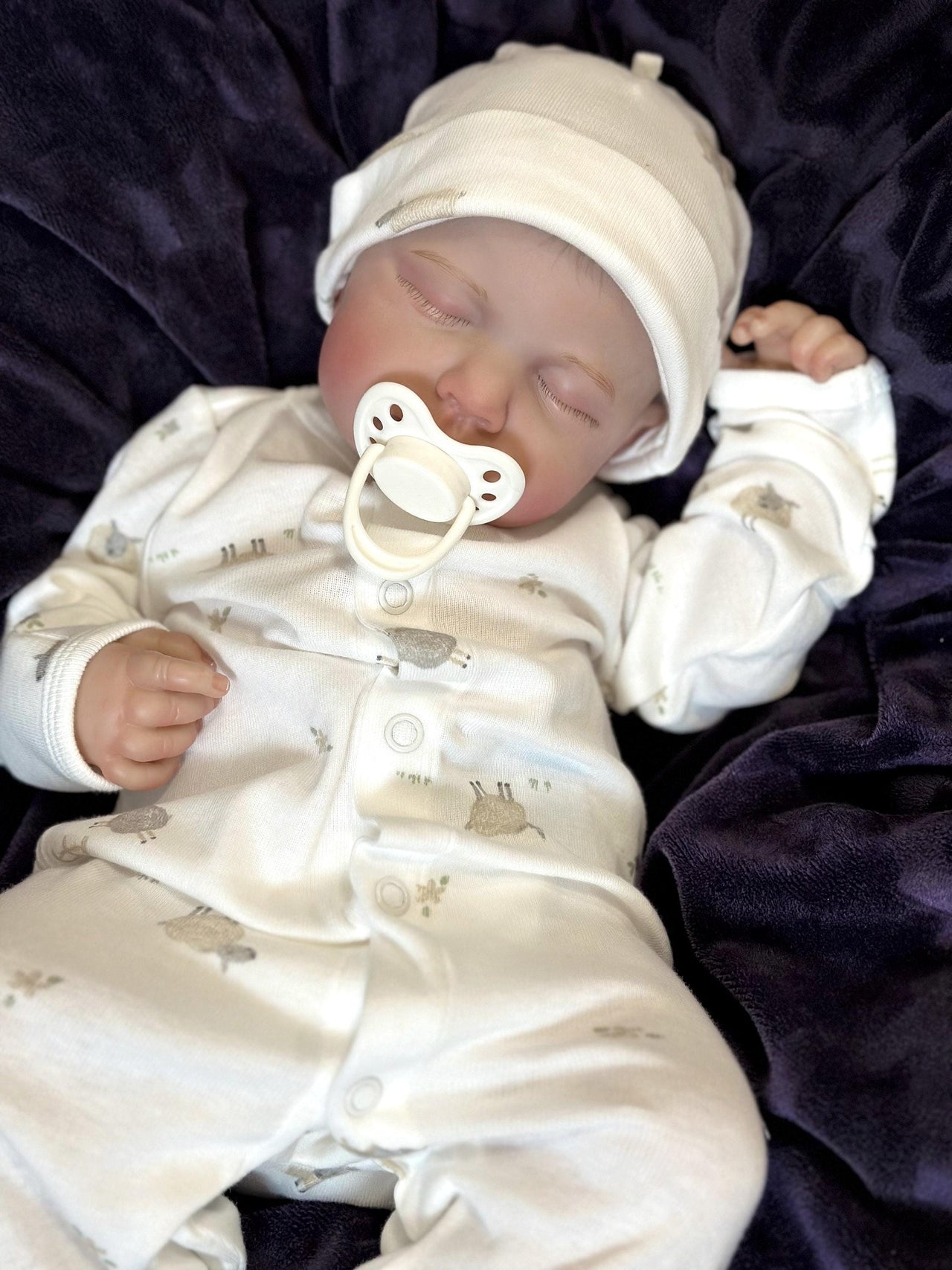 A baby doll lying on a cozy blanket, with a pacifier placed nearby.