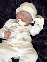 Thumbnail for A baby doll lying on a cozy blanket, with a pacifier placed nearby.