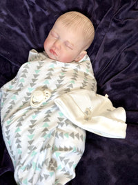 Thumbnail for A baby doll rests on a soft blanket, showcasing its delicate features and clothing.