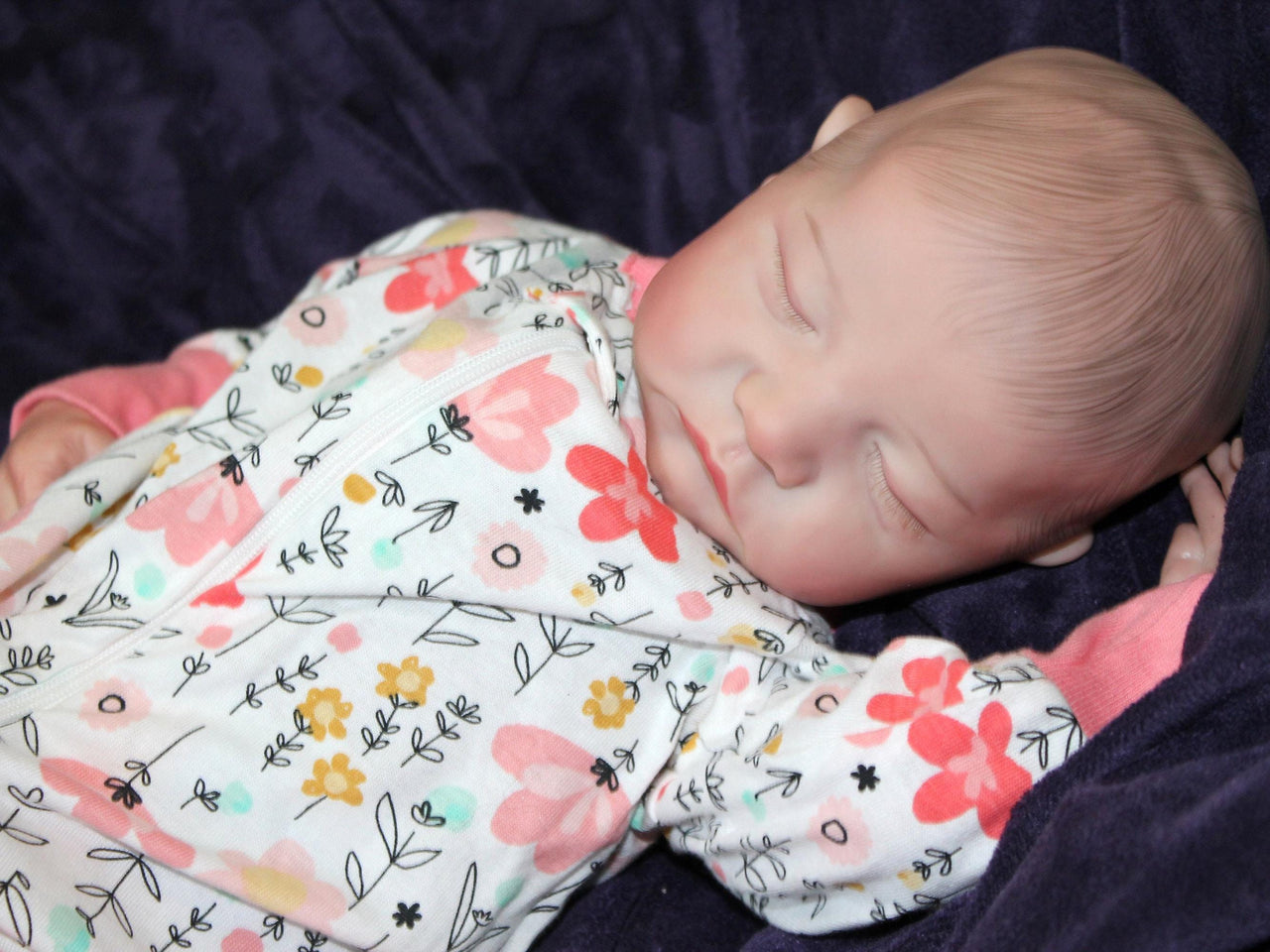A baby in pink floral pajamas peacefully lying down on a soft surface.