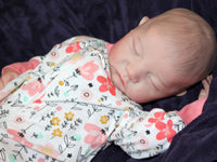 Thumbnail for A baby in pink floral pajamas peacefully lying down on a soft surface.