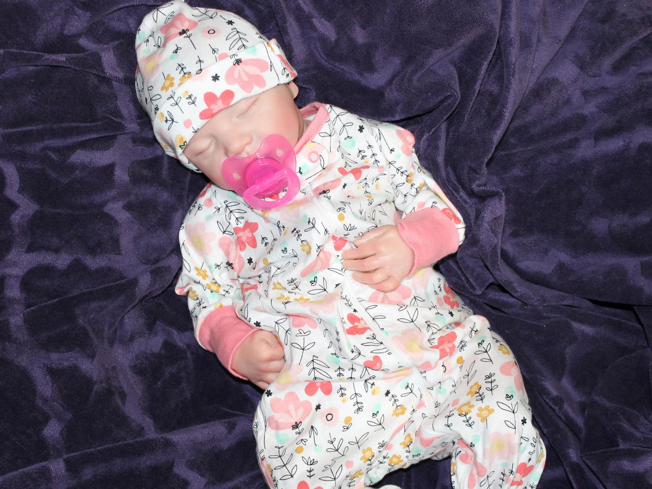 A baby in pink floral pajamas peacefully lying down on a soft surface.