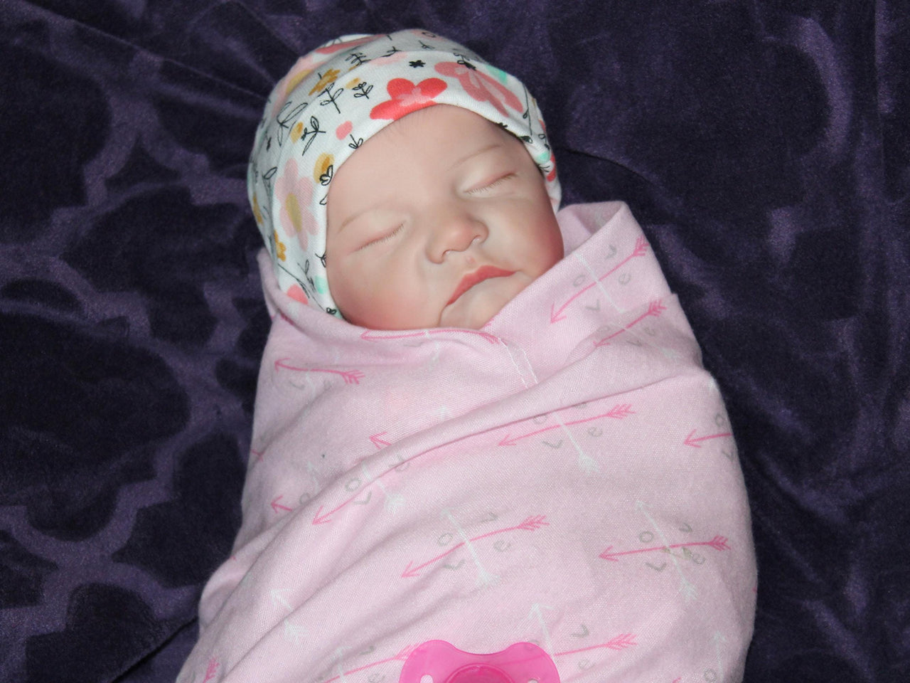A baby in cozy pink blanket, resting on their back with a calm demeanor.
