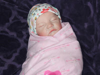 Thumbnail for A baby in cozy pink blanket, resting on their back with a calm demeanor.