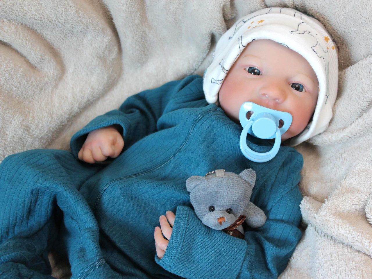 A baby doll rests on a soft blanket beside a cuddly teddy bear, creating a cozy and playful scene.