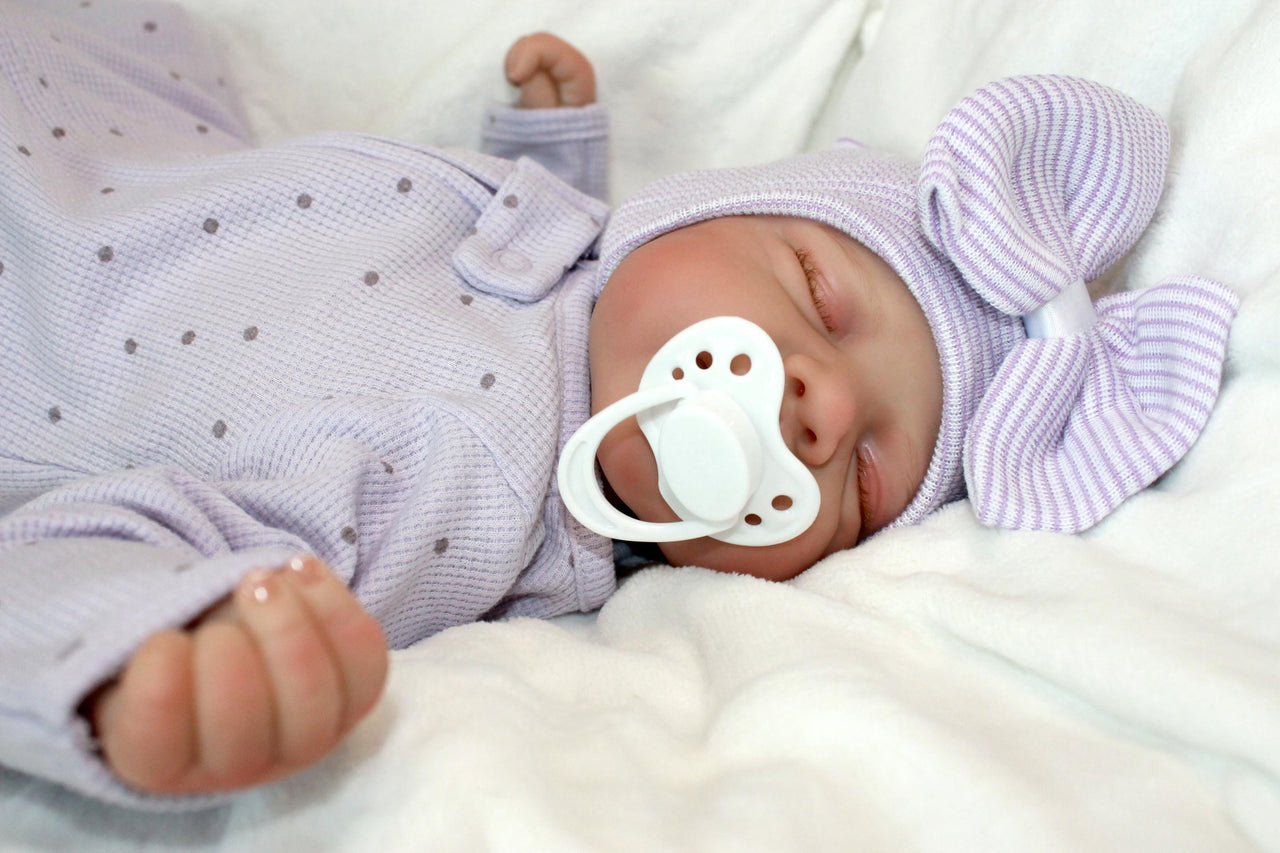 A baby doll with a pacifier lies on a bed, showcasing its soft features and gentle expression.