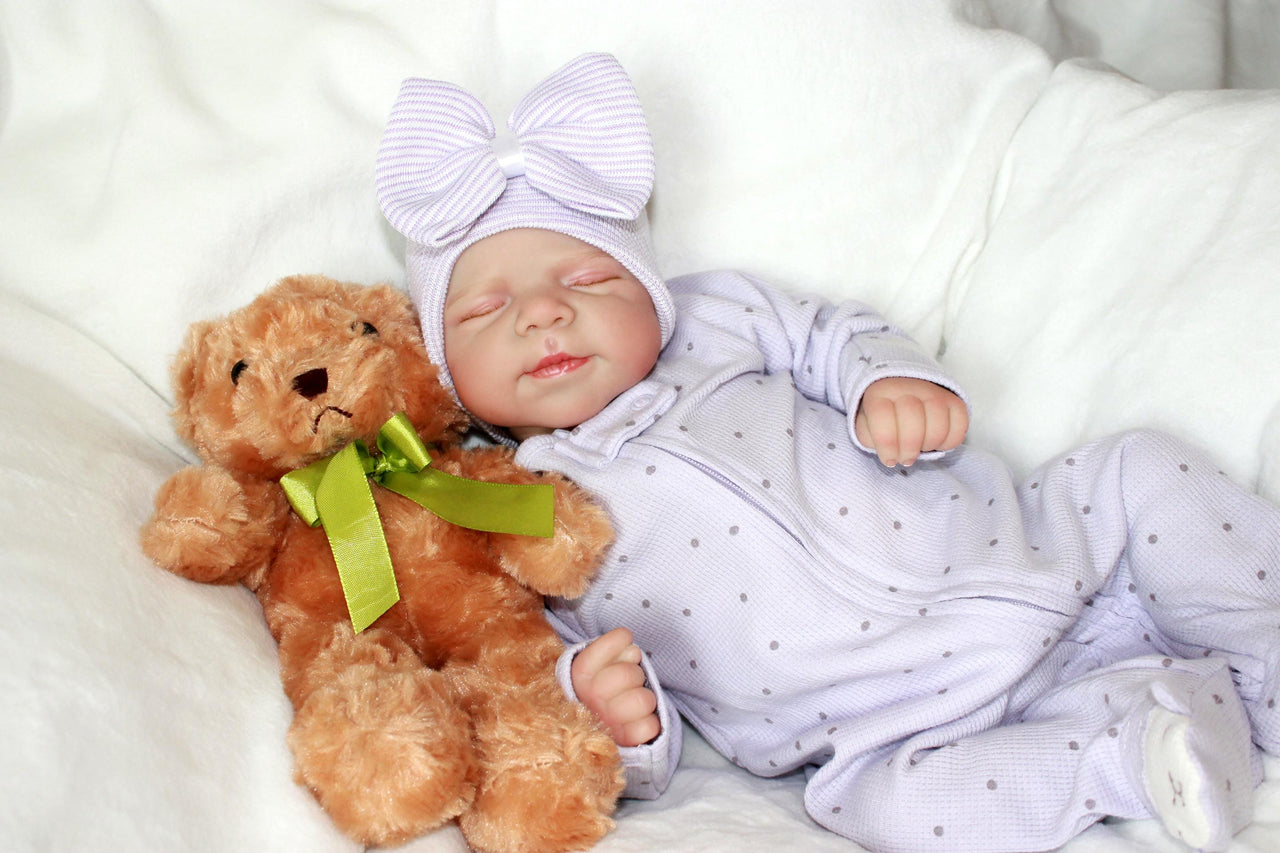 A baby doll lying on a patterned blanket, emphasizing its cute expression and attire.