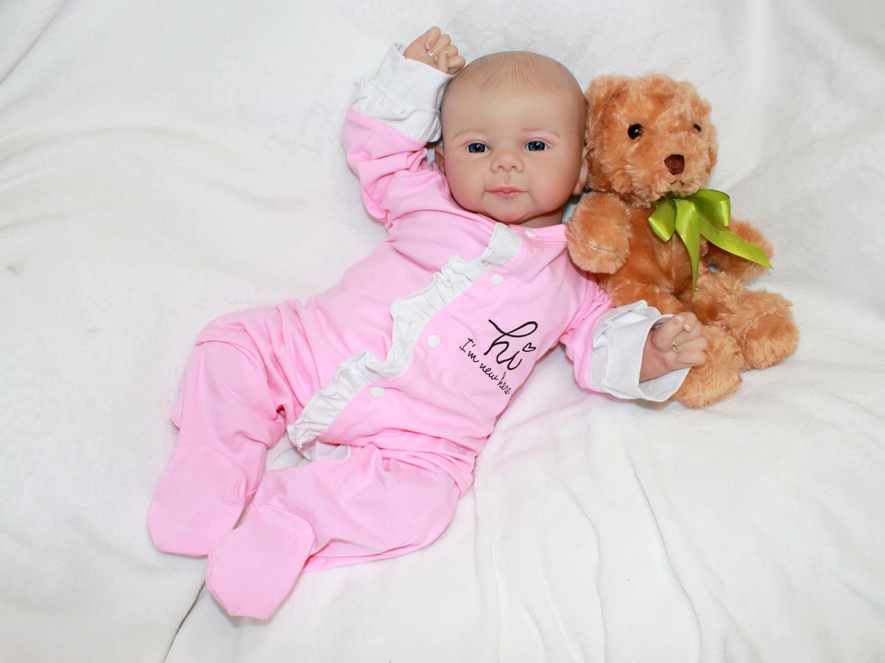 A baby doll rests on a white blanket beside a soft teddy bear, creating a cozy and playful scene.