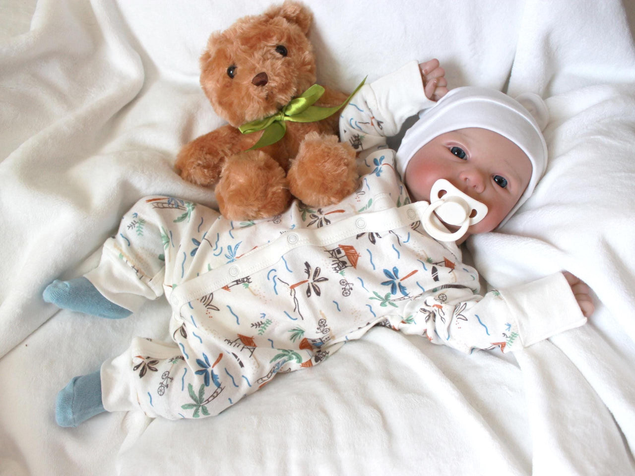 A baby doll positioned on a clean white sheet, with a pacifier, highlighting its charming design and soft textures.