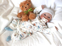 Thumbnail for A baby doll is positioned on a white blanket next to a teddy bear, symbolizing warmth and companionship in a serene setting.