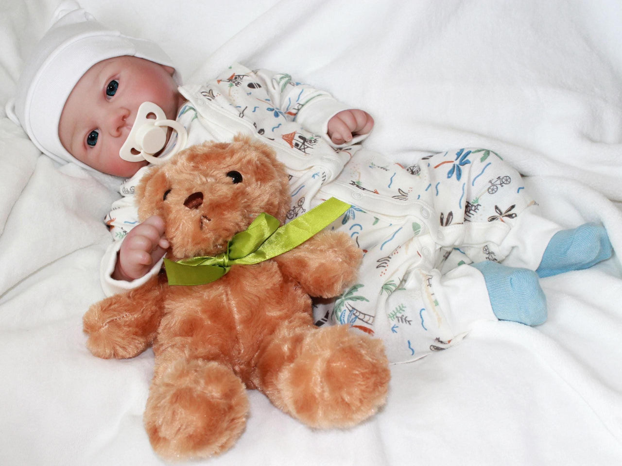 A baby doll is positioned on a white blanket next to a teddy bear, symbolizing warmth and companionship in a serene setting.