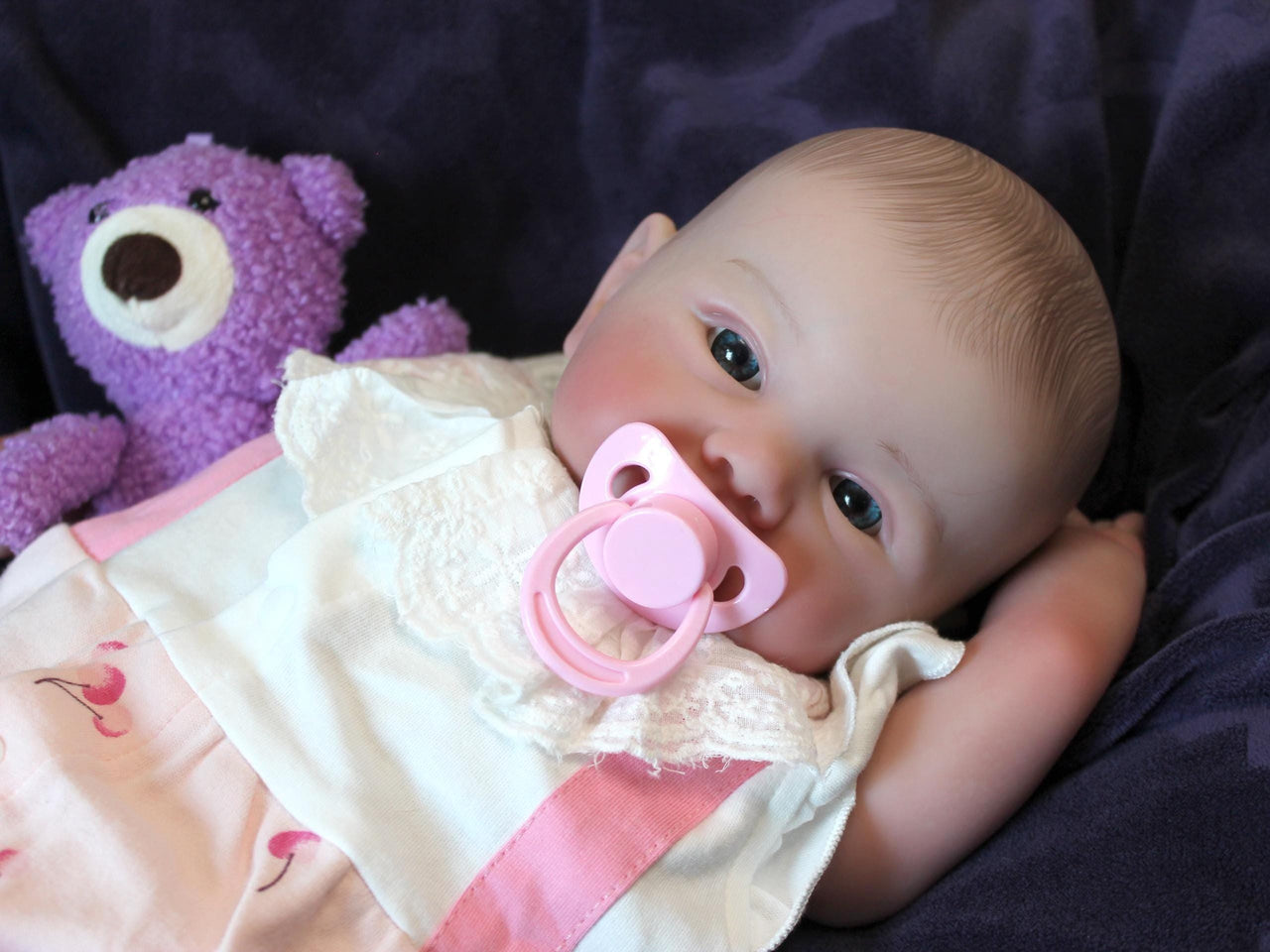 A baby doll positioned on a clean purple sheet, highlighting its charming design and soft textures.