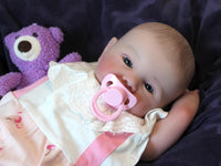 Thumbnail for A baby doll positioned on a clean purple sheet, highlighting its charming design and soft textures.