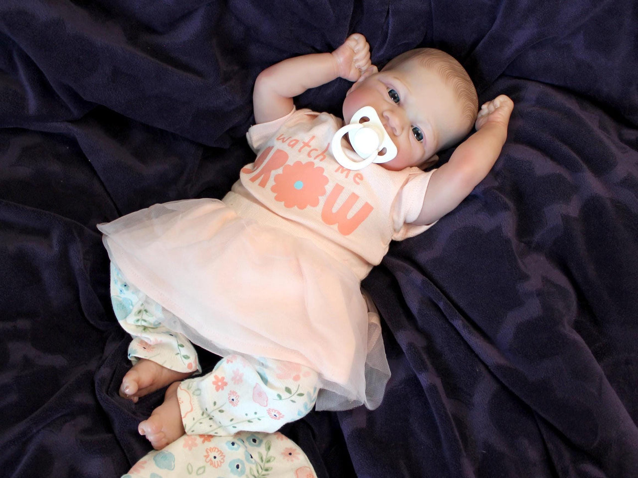 A baby doll with a pacifier rests on a soft blanket, showcasing its delicate features and gentle expression.