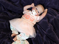 Thumbnail for A baby doll with a pacifier rests on a soft blanket, showcasing its delicate features and gentle expression.