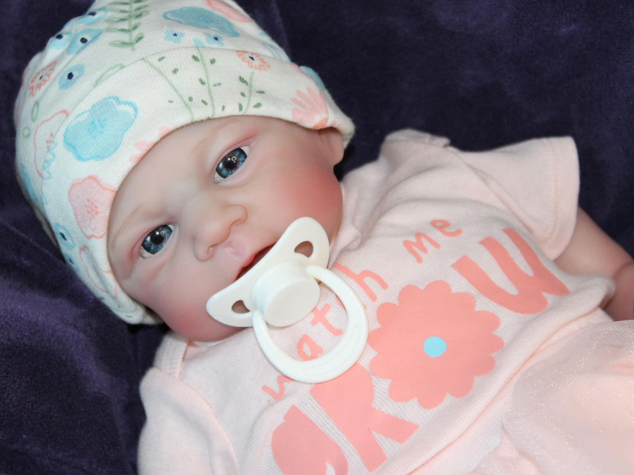 A baby doll with a pacifier rests on a soft blanket, showcasing its delicate features and gentle expression.