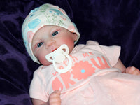 Thumbnail for A baby doll with a pacifier rests on a soft blanket, showcasing its delicate features and gentle expression.