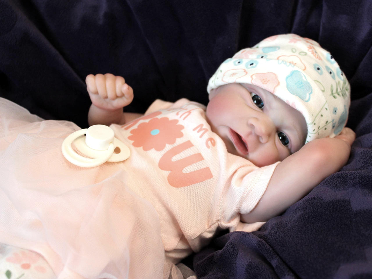 A baby doll in a pink dress and hat, posed cutely with a gentle smile, highlighting its charming design.