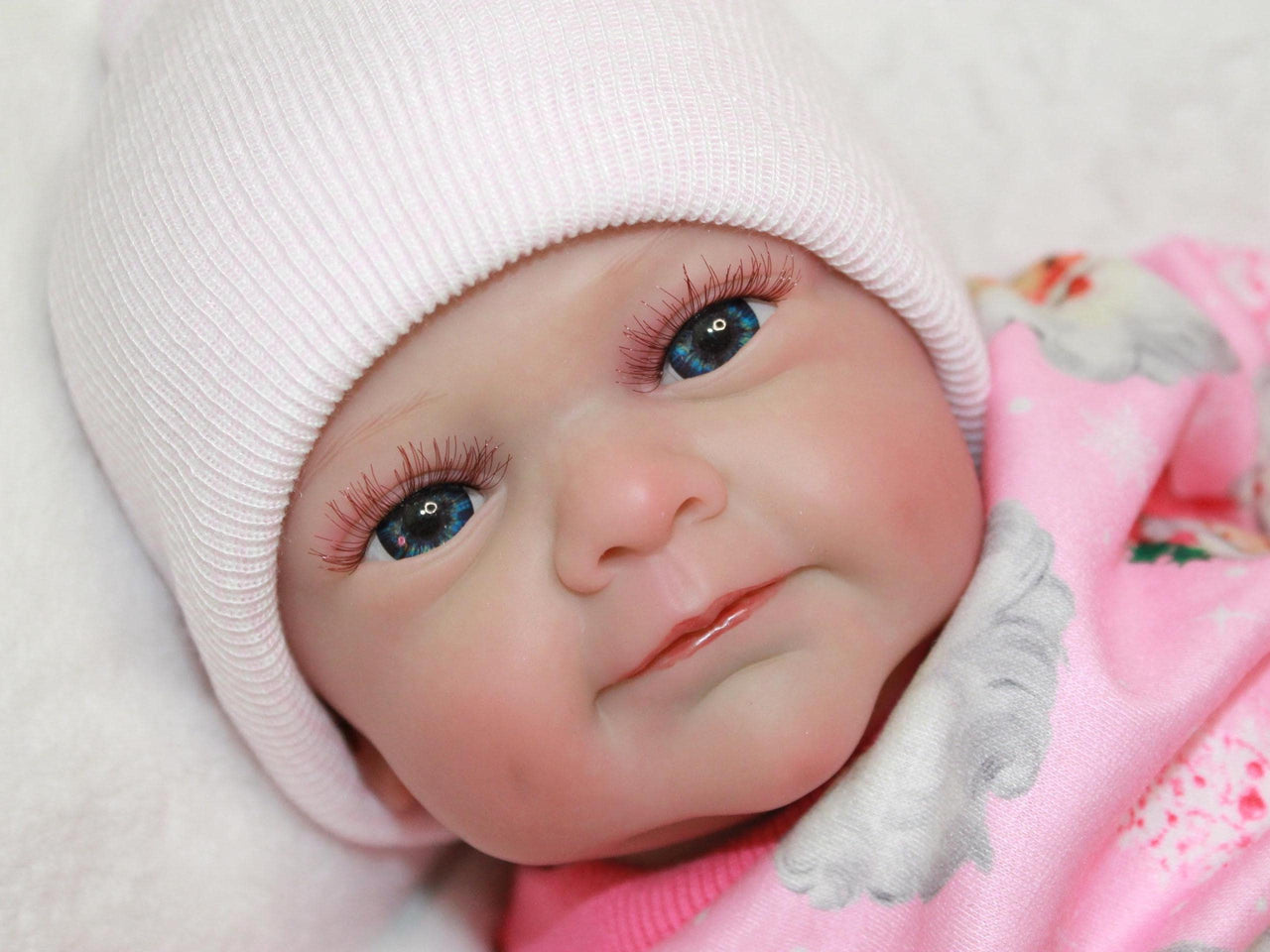 A baby doll wearing pink pajamas is positioned on a bed, highlighting a serene and nurturing environment.