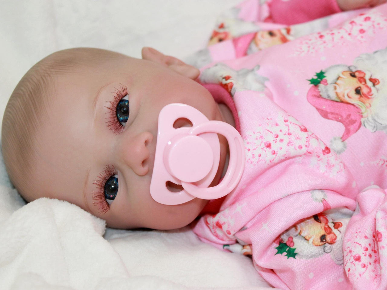 A baby doll with a pacifier rests on a soft bed, showcasing its delicate features and cozy surroundings.