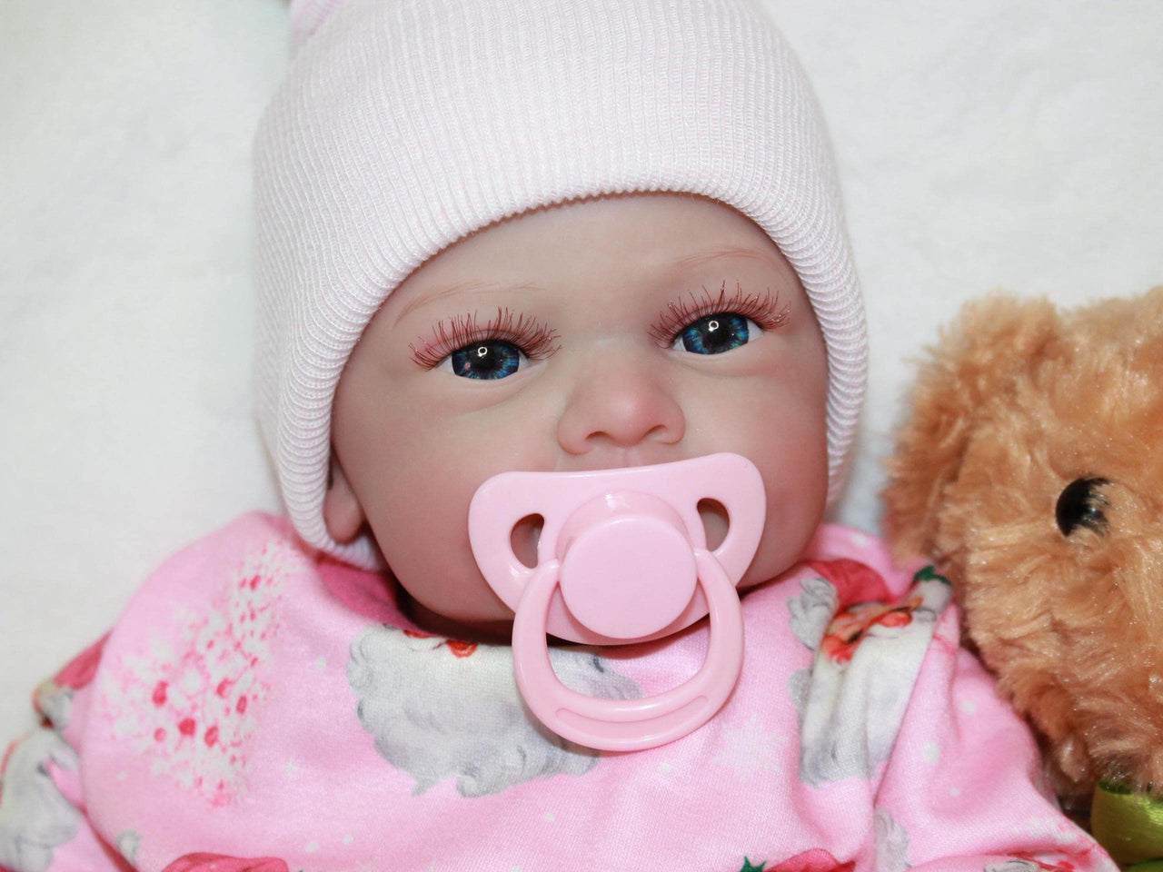 A baby doll with a pacifier rests on a soft bed, showcasing its delicate features and cozy surroundings.