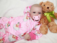 Thumbnail for A baby doll with a pacifier rests on a soft bed, showcasing its delicate features and cozy surroundings.