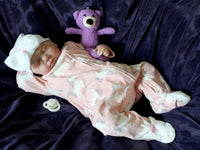 Thumbnail for A baby doll resting on a soft purple couch, showcasing its delicate features and bright clothing.