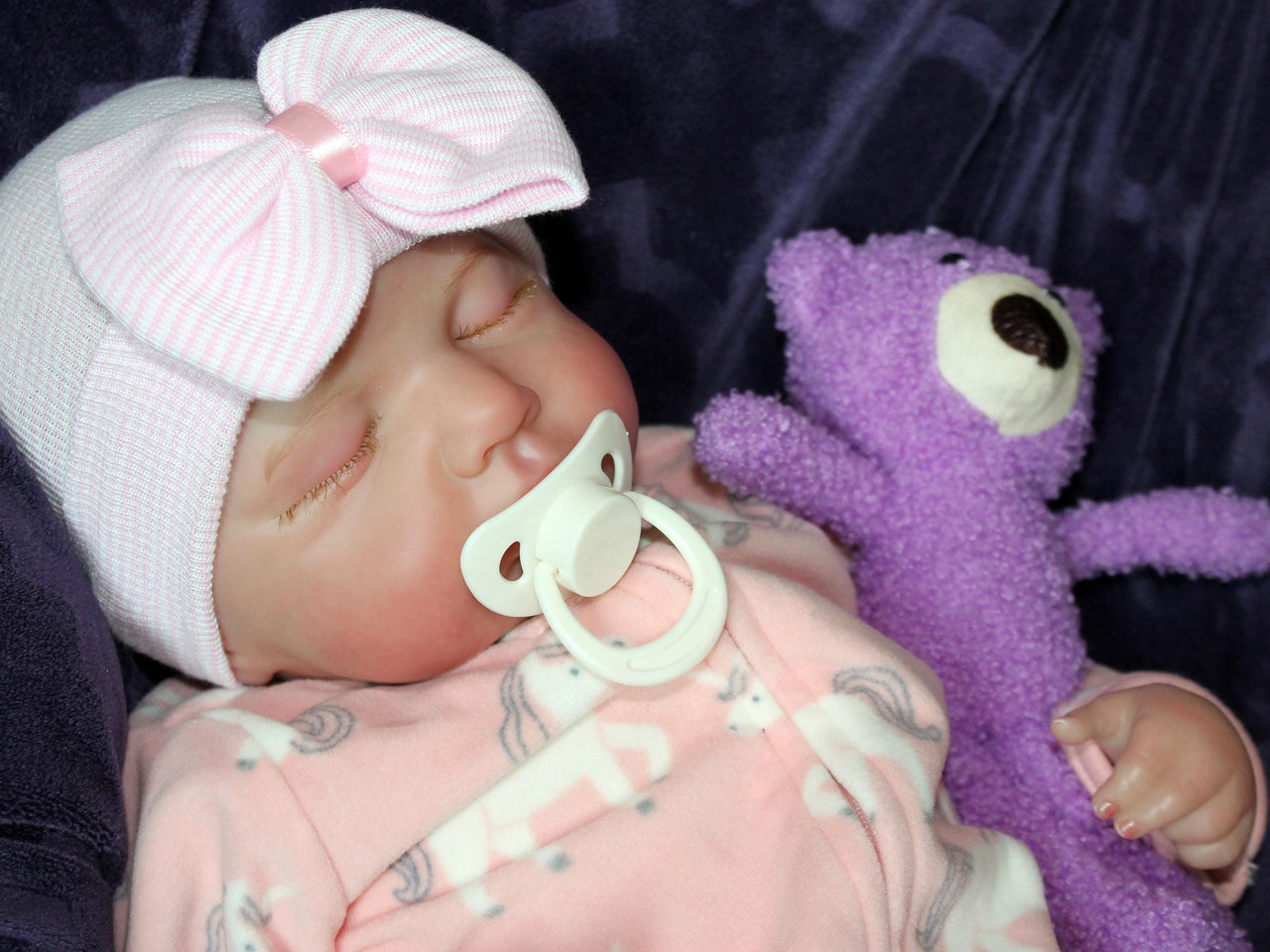 A baby doll lying on a cozy purple couch, emphasizing its cute appearance and colorful attire.