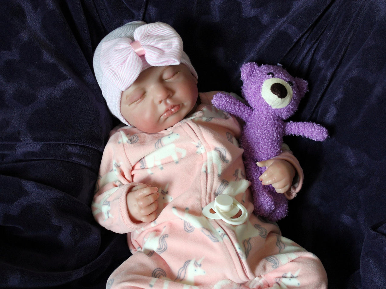 A baby doll lying on a cozy purple couch, emphasizing its cute appearance and colorful attire.