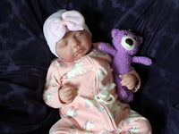 Thumbnail for A baby doll lying on a cozy purple couch, emphasizing its cute appearance and colorful attire.