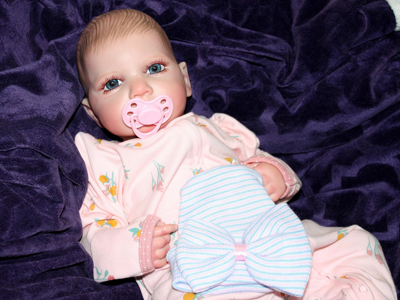 Realistic reborn baby doll dressed in pink floral pajamas with pacifier, cuddly lifelike doll for kids to play and nurture