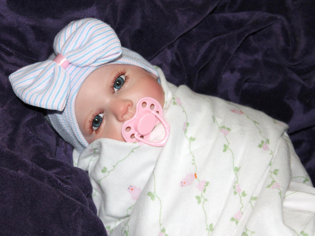 Realistic reborn baby doll dressed in pink floral pajamas with pacifier, cuddly lifelike doll for kids to play and nurture