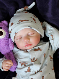 Thumbnail for Sleeping reborn baby doll in fox-print pajamas with matching hat, holding a purple teddy bear, lifelike newborn with white pacifier